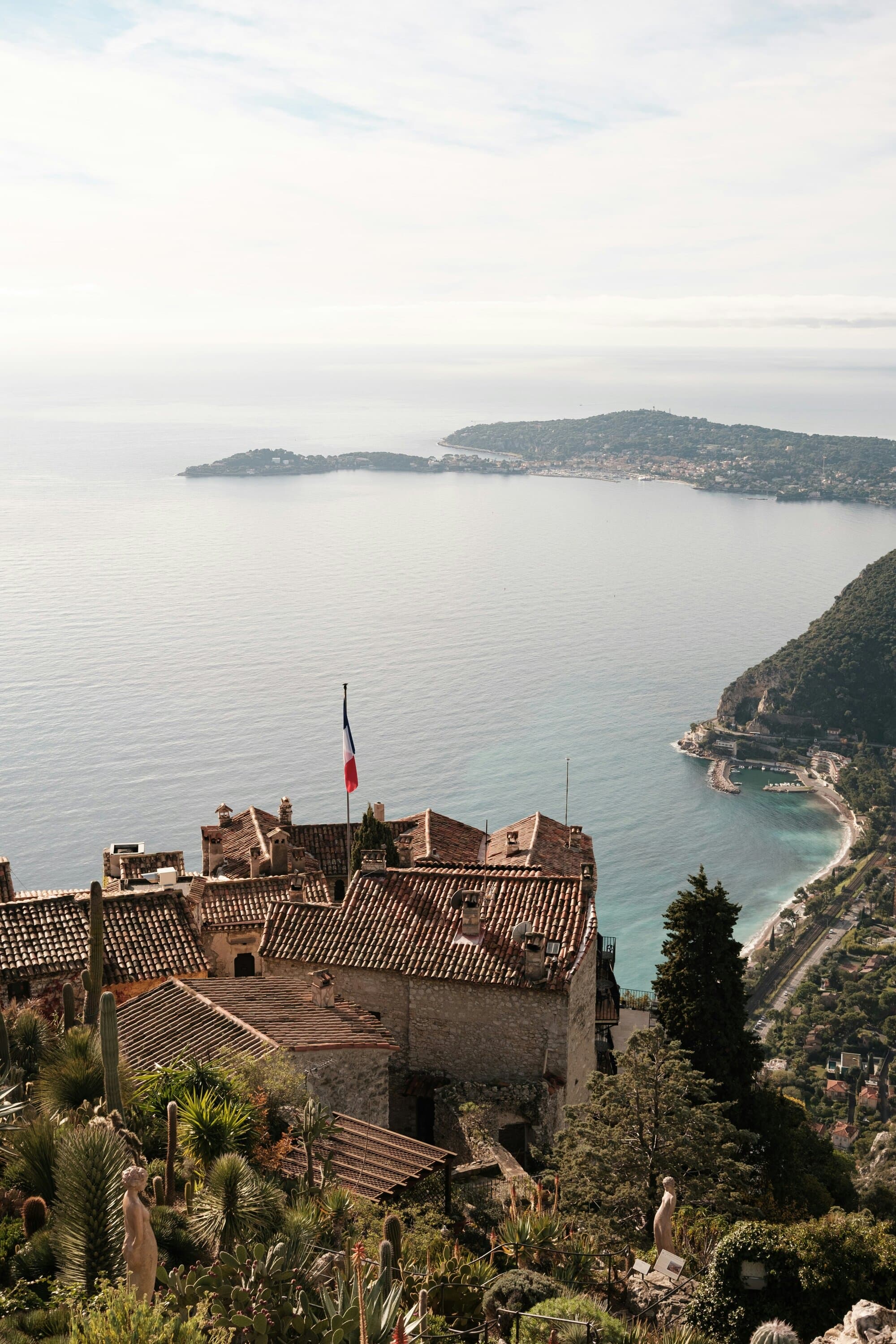 Èze rooftops with the French flag and the bay below — the medieval village Frank Martin tears through in The Transporter.